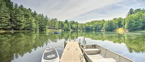 A wooden dock extending into calm water with boats docked, surrounded by dense forest.