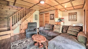 A cozy living room with a wooden staircase, a gray sofa set, and a patterned rug.