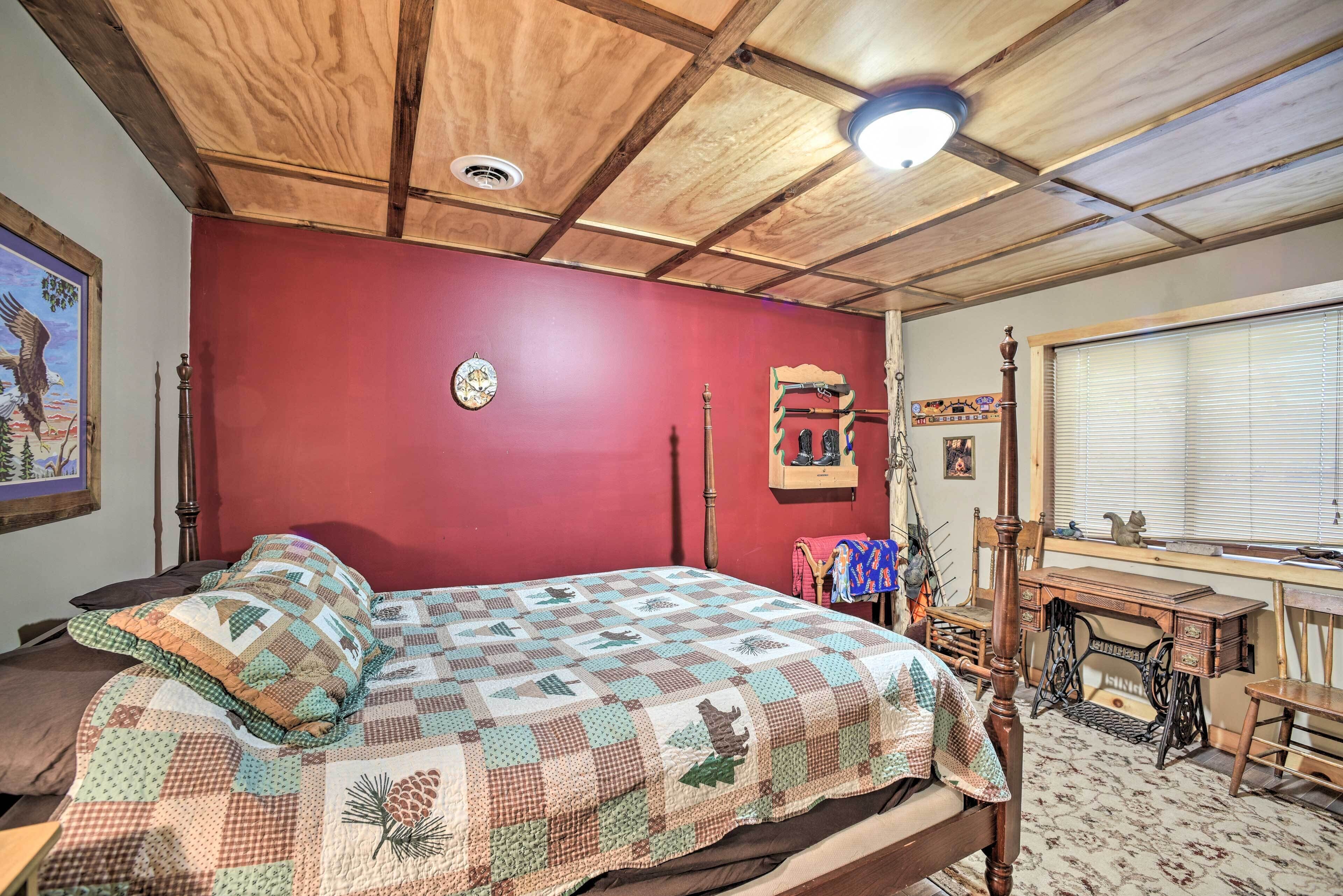 Een slaapkamer met een houten plafond, een rode wand, een geborduurde spreidekbed en een houten bureau, plus een raam met zonwering.