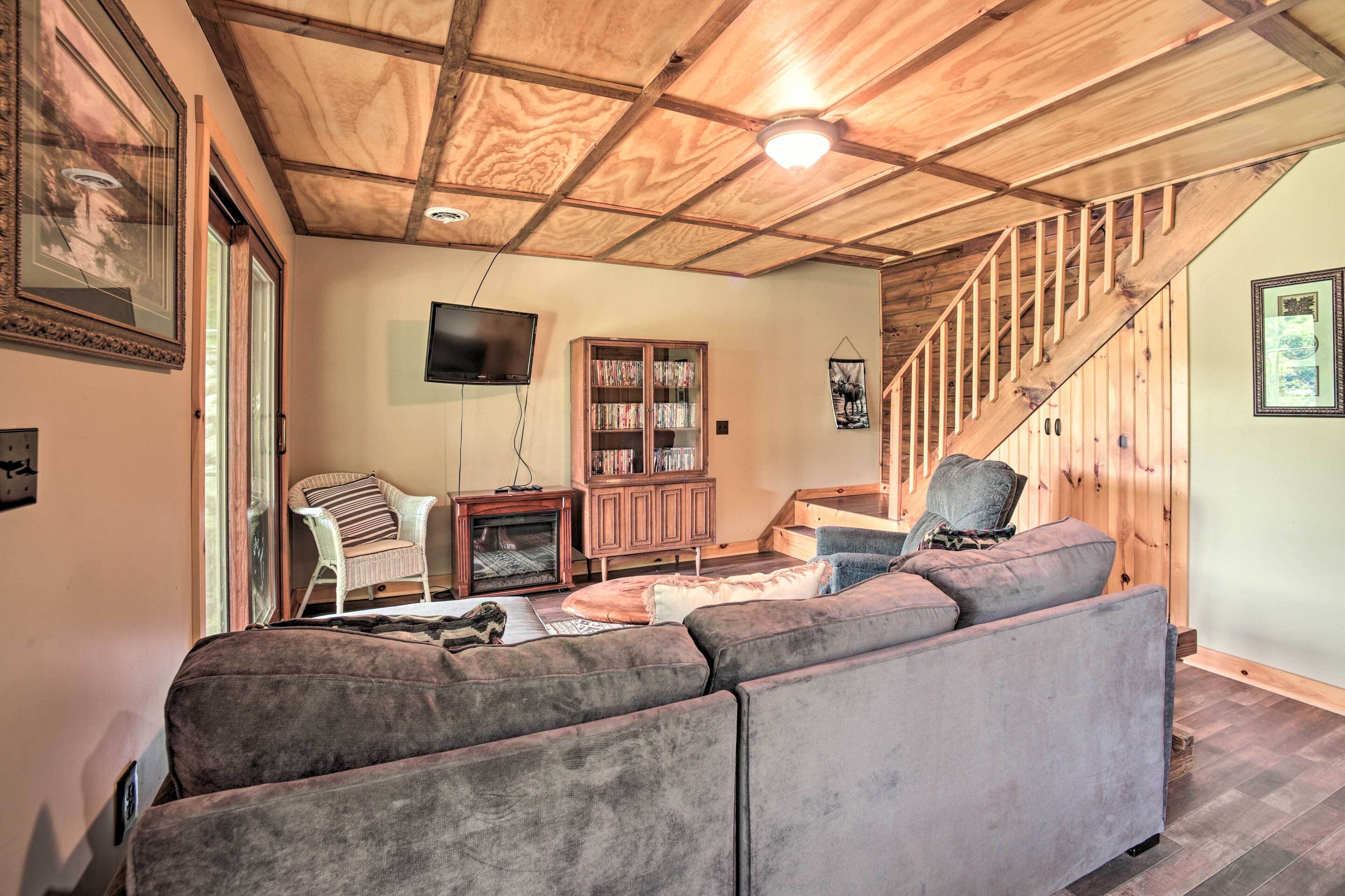 Una sala de estar acogedora con techo de madera, chimenea, televisor, estantería y una escalera.