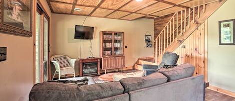Una sala de estar acogedora con techo de madera, chimenea, televisor, estantería y una escalera.