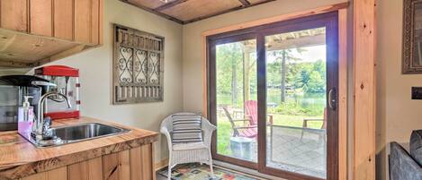A wooden interior with a kitchen area, a chair near a sliding glass door, and a view of the outdoors.