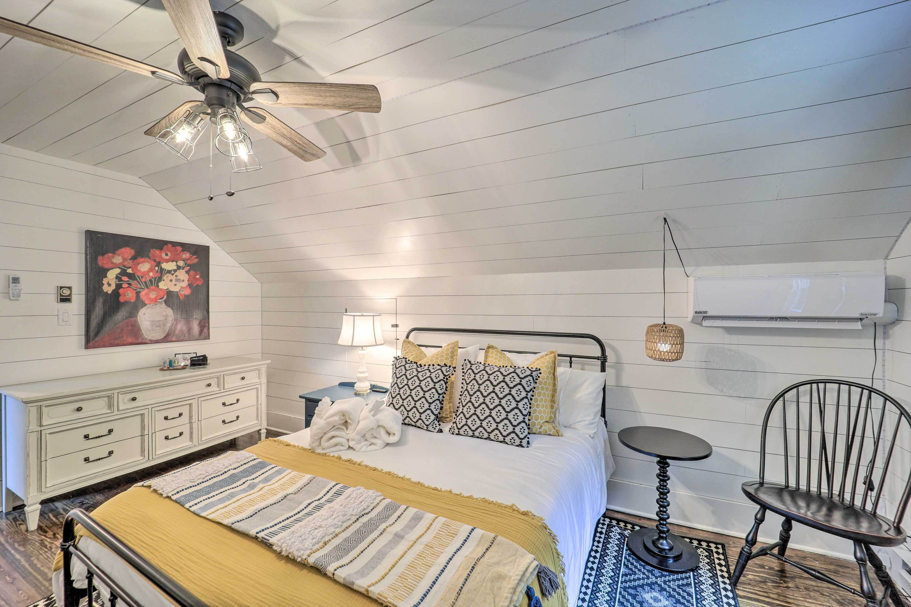 A bedroom with a bed, a nightstand, a chair, a ceiling fan, and a wall-mounted air conditioner.
