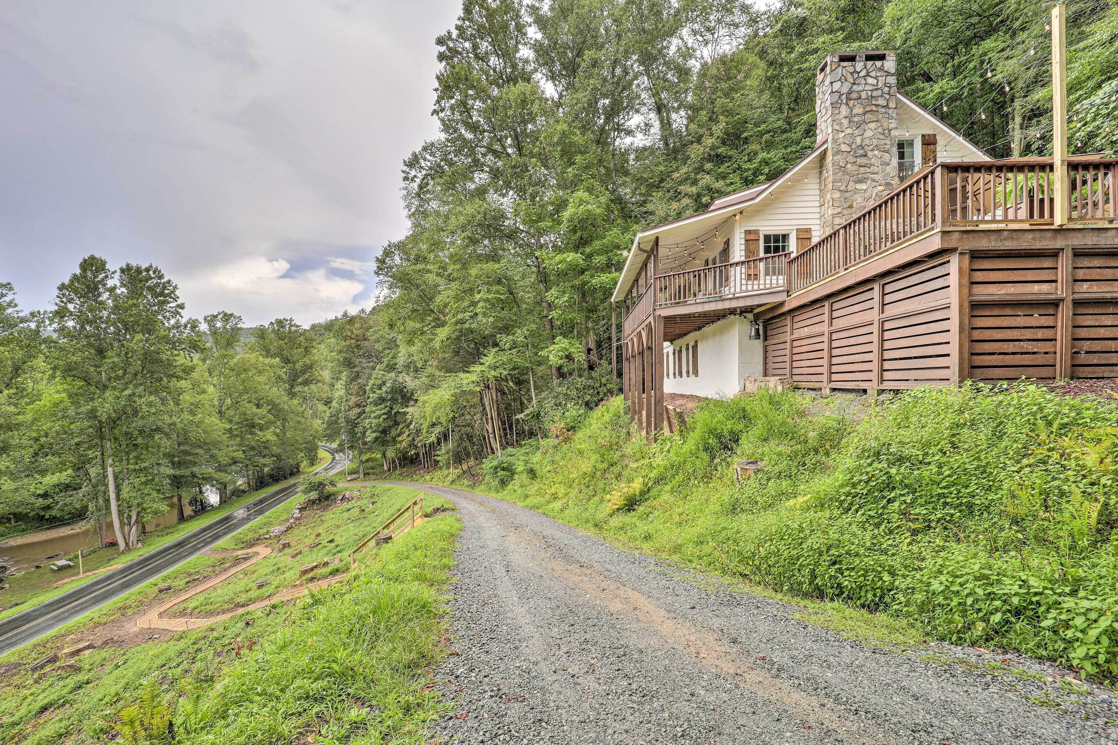 Une maison avec une cheminée en pierre, une terrasse en bois et une allée gravillonnée.