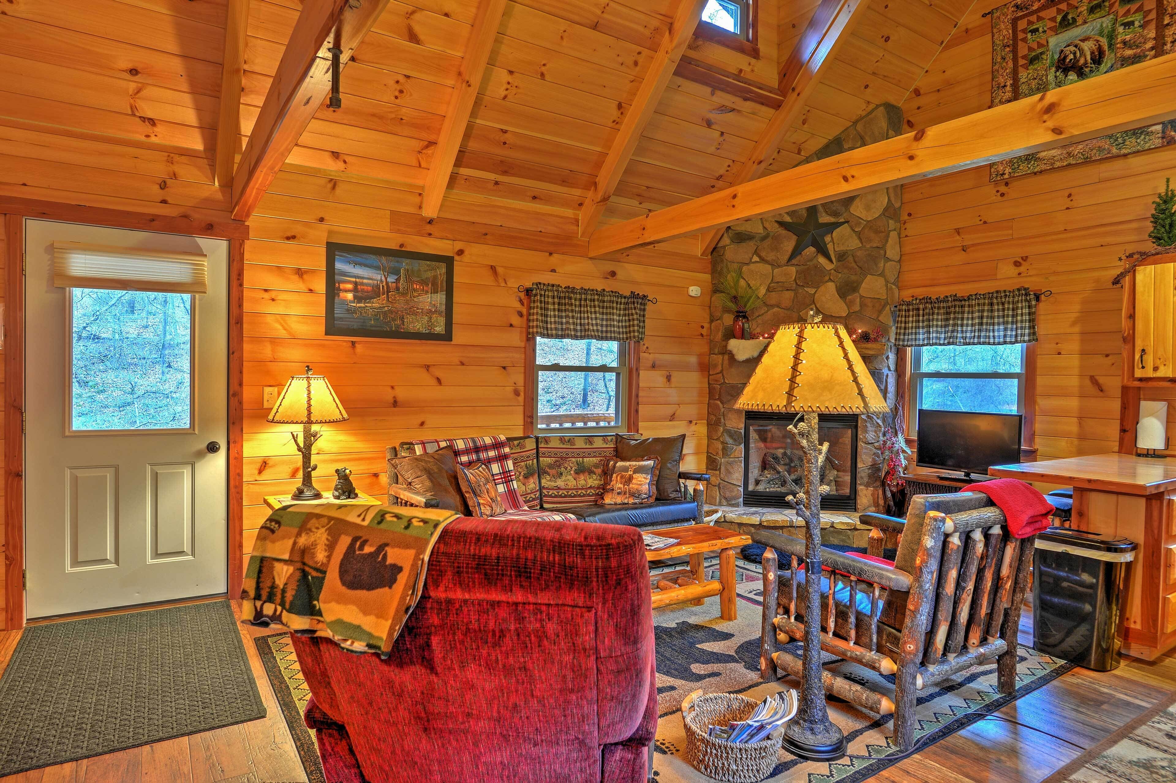 A cozy log cabin interior with a fireplace, wooden furniture, and a stone accent wall.