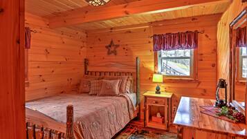 A cozy wooden cabin bedroom with a bed, a nightstand, a lamp, and a window with curtains.