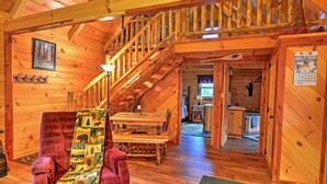 A wooden cabin interior with a dining area, a staircase, and a kitchen. - Rustic Dundee Log Cabin w/ Hot Tub & Forest Views! (Dundee)