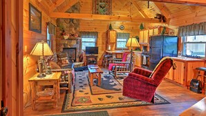 A cozy cabin interior with a wooden interior, a fireplace, a dining area, and a kitchen. - Rustic Dundee Log Cabin w/ Hot Tub & Forest Views! (Dundee)