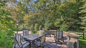 An outdoor patio with a stone table and chairs, surrounded by lush greenery and trees.