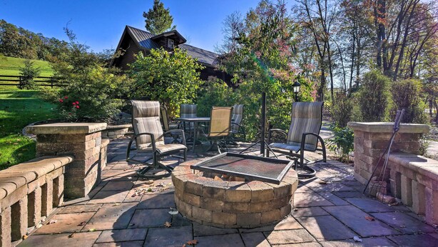 A patio with stone seating, a fire pit, and a view of a rustic house. - Rustic Dundee Log Cabin w/ Hot Tub & Forest Views! (Dundee)