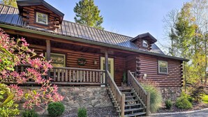 A log cabin with a stone foundation, a porch with a railing, and a staircase leading to the entrance. - Rustic Dundee Log Cabin w/ Hot Tub & Forest Views! (Dundee)