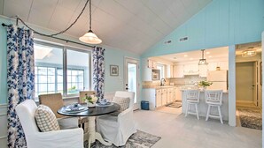 A spacious kitchen with white cabinets, a dining area with a round table and white chairs, and a large window with blue floral curtains. - Refreshing Colonial Beach Vacation Rental! (Colonial Beach)