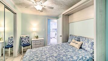 Une chambre avec un grand lit, un ventilateur de plafond, une table de chevet, une chaise et une porte donnant sur une salle de bain.