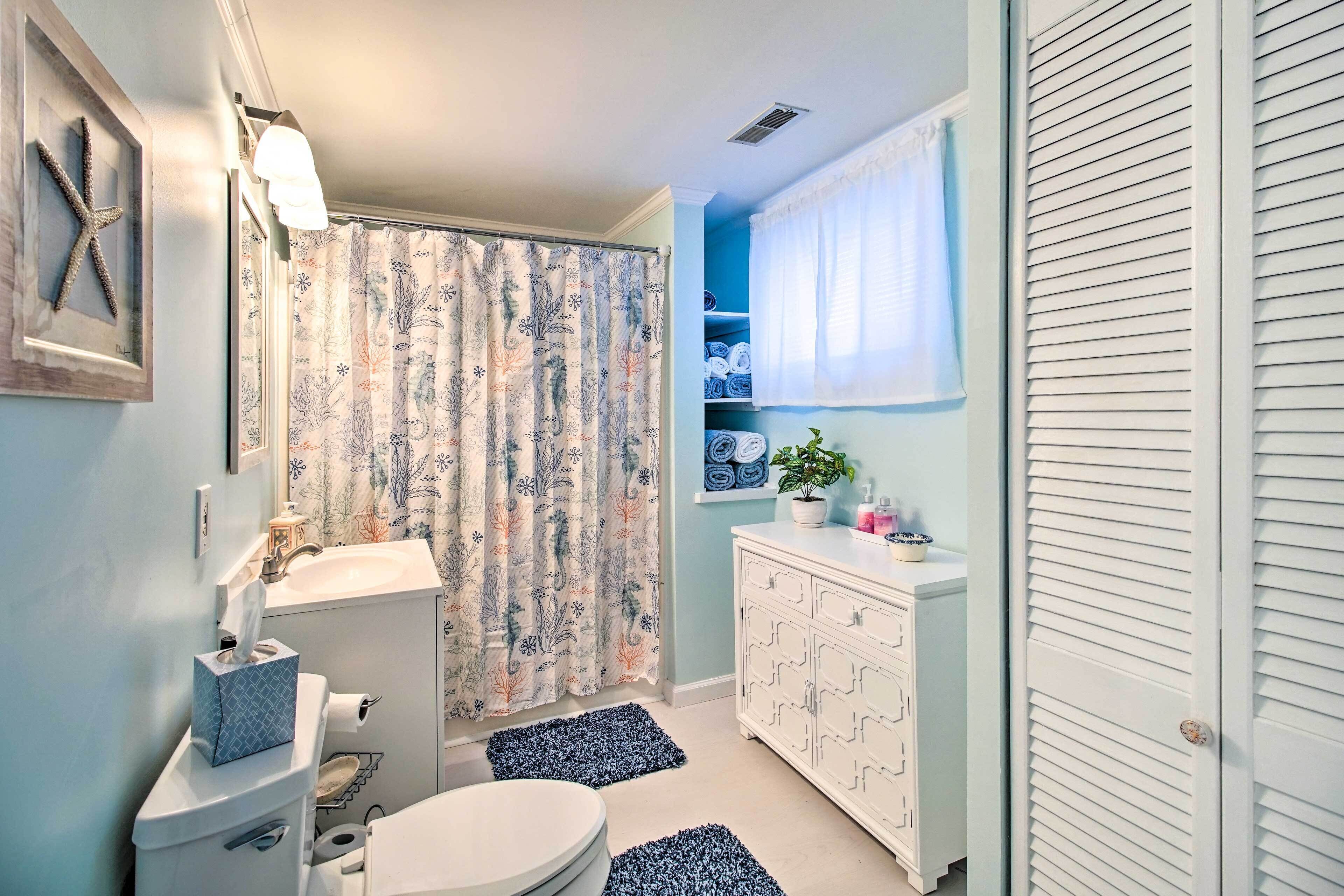 Een badkamer met toilet, wastafel en douchegordijn. Er is een witte kast met lades en een plantje bovenop.