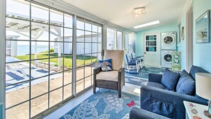 A sunlit room with large windows, a wicker chair, a blue sofa, and a laundry area with a washing machine. - Refreshing Colonial Beach Vacation Rental! (Colonial Beach)