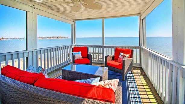 A covered outdoor seating area with wicker furniture and red cushions, overlooking a body of water. - Refreshing Colonial Beach Vacation Rental! (Colonial Beach)
