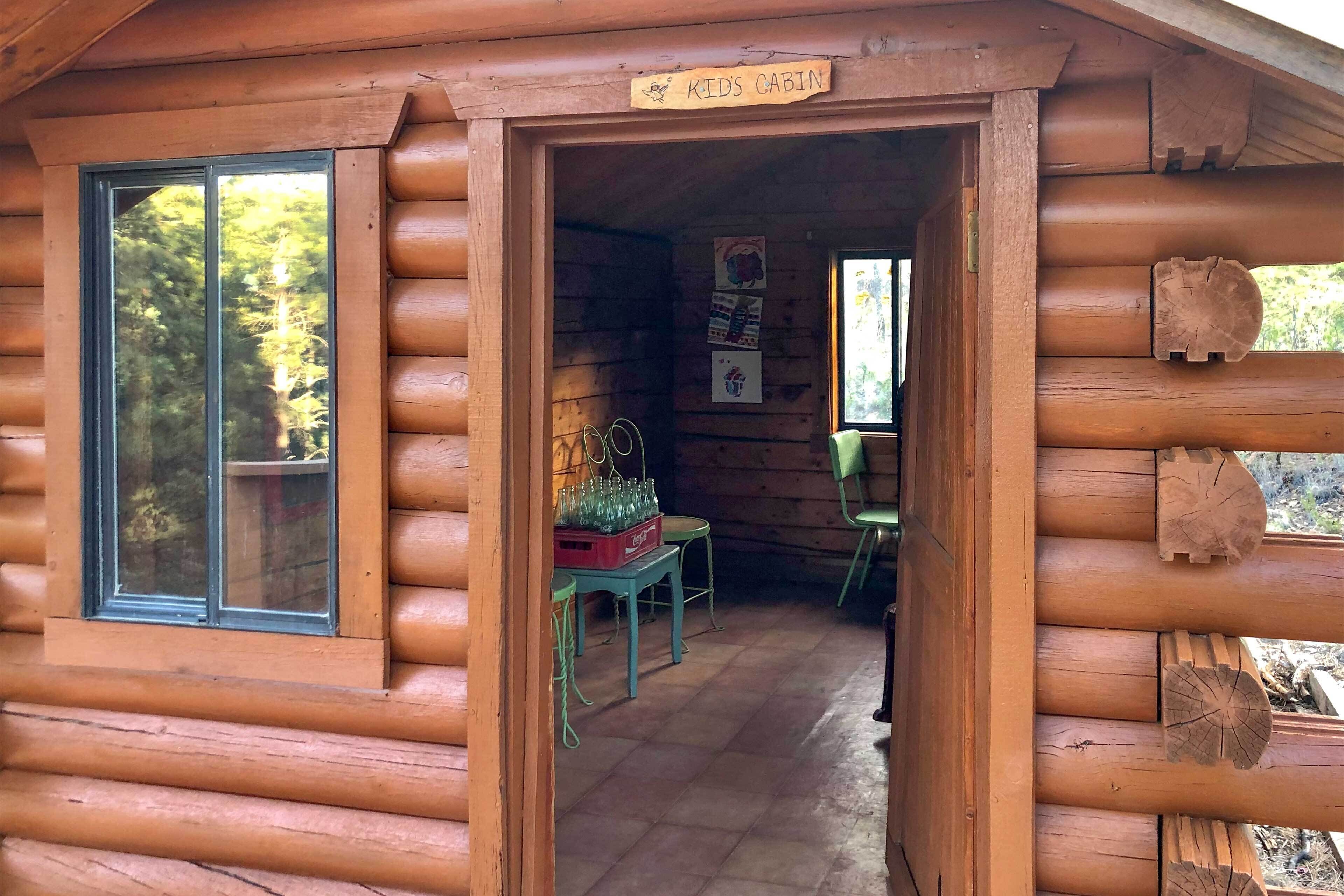 A log cabin with a children's cabin sign, a window, a table with chairs, and artwork on the wall.