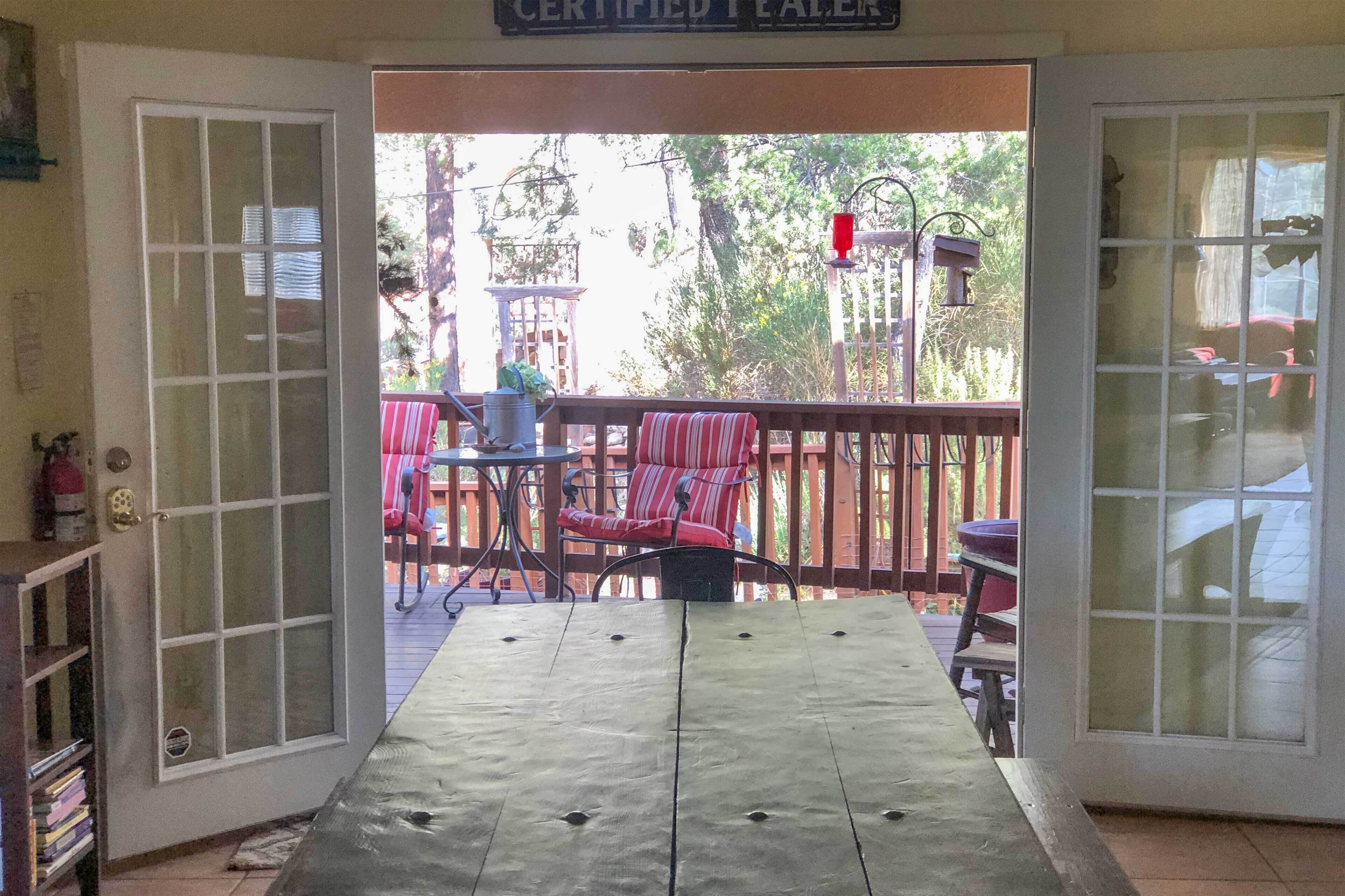 An open door leading to an outdoor patio with a table and chairs, a sign above the door, and a view of trees and a building in the background.