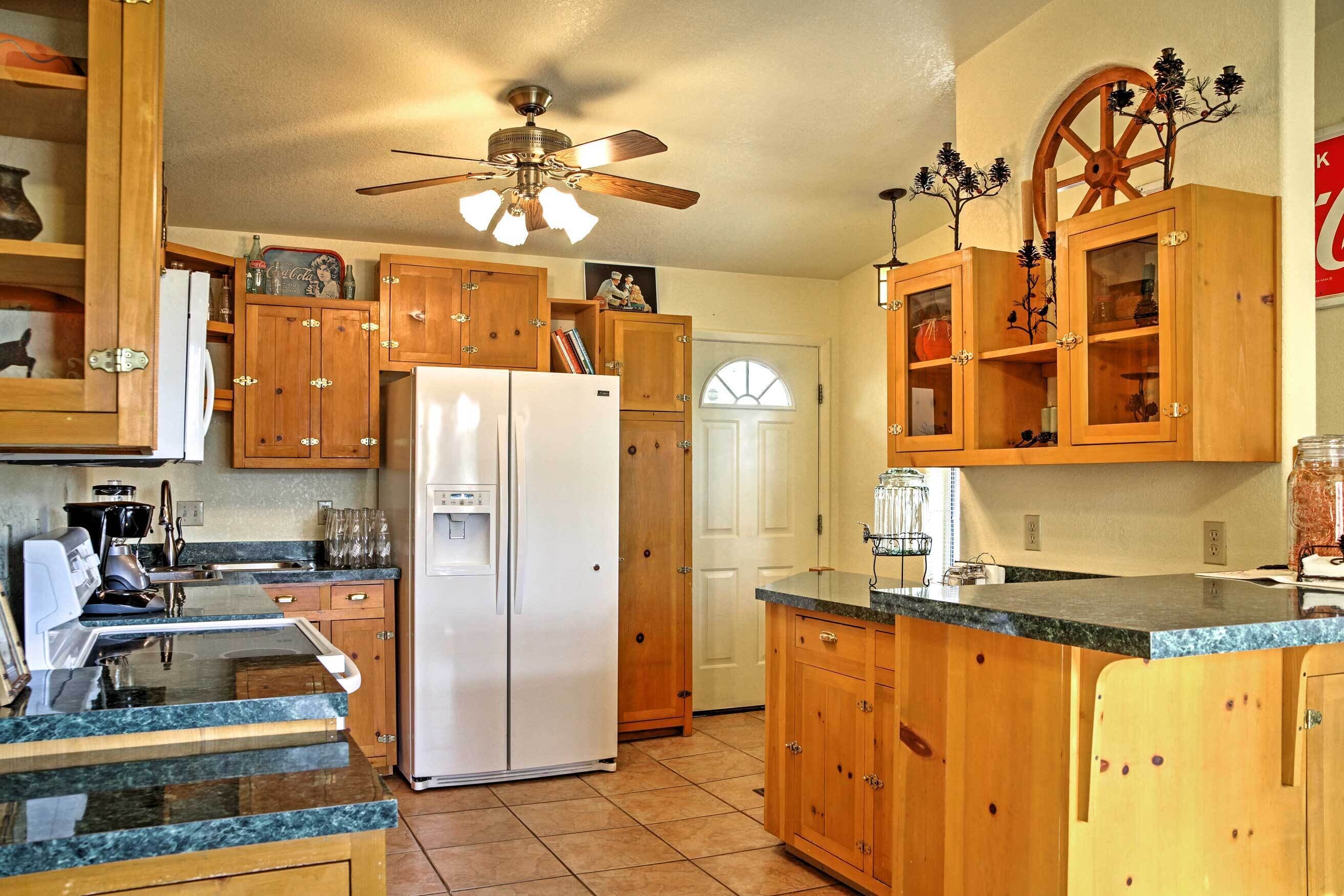 A kitchen with wooden cabinets, a white refrigerator, granite countertops, and a ceiling fan.