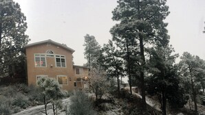 A two-story house with a brown exterior, surrounded by snow-covered trees and shrubs. - Quiet Ruidoso Hideaway - 2 Mi to Grindstone Lake! (Ruidoso)