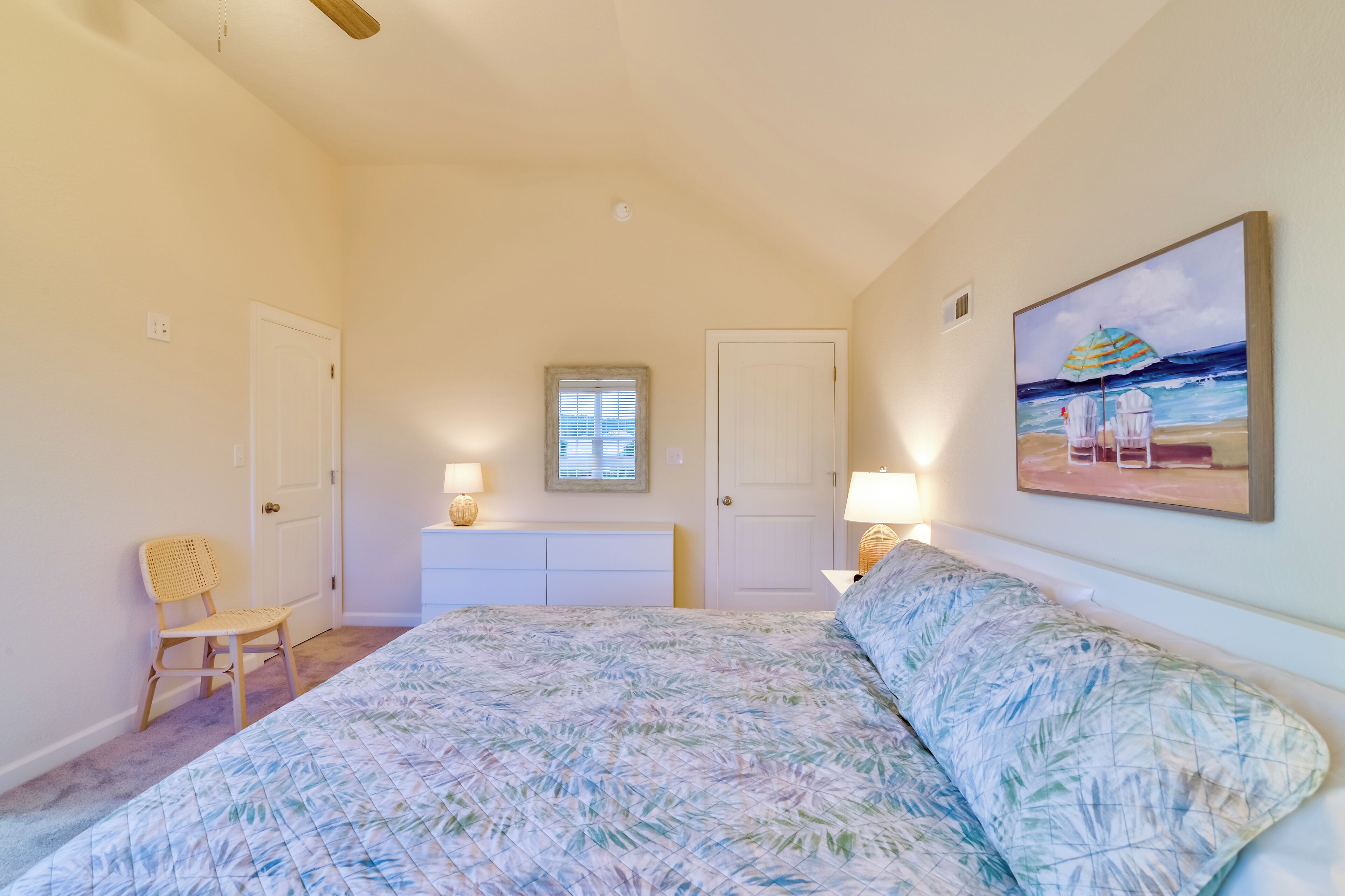 A bedroom with a bed, a chair, a dresser, and a painting of a beach scene.