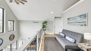 Um interior moderno com um sofá cinzento, um ventilador de teto de madeira e uma janela grande.