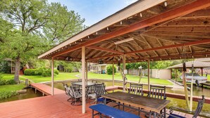 Un patio techado al aire libre con una mesa y sillas de madera, un estanque pequeño y un embarcadero.
