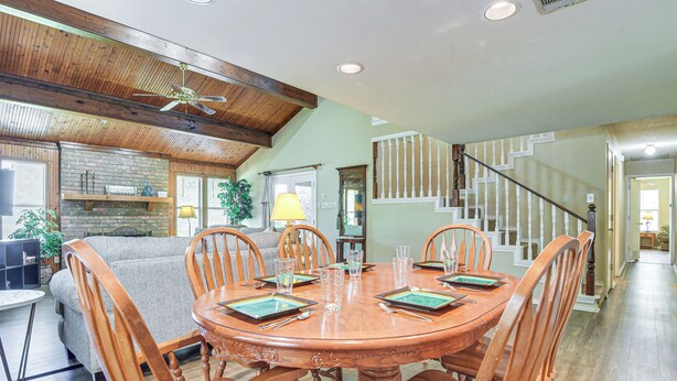 A dining area with a wooden table and chairs, a brick wall, and a staircase in the background.