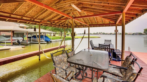 Un muelle techado con una mesa y sillas, un bote y vistas al agua.