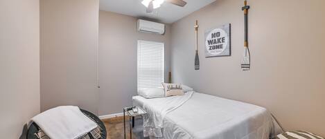 A bedroom with a bed, a ceiling fan, a window with blinds, a wall-mounted air conditioner, and a motivational poster.