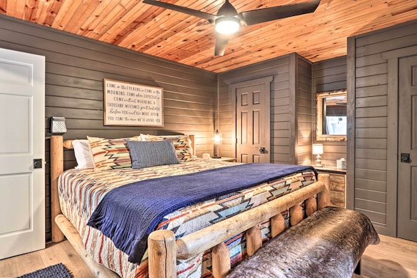 Une chambre avec un plafond en bois, un lit recouvert d’une courtepointe aux couleurs vives, un banc et un panneau fixé au mur.