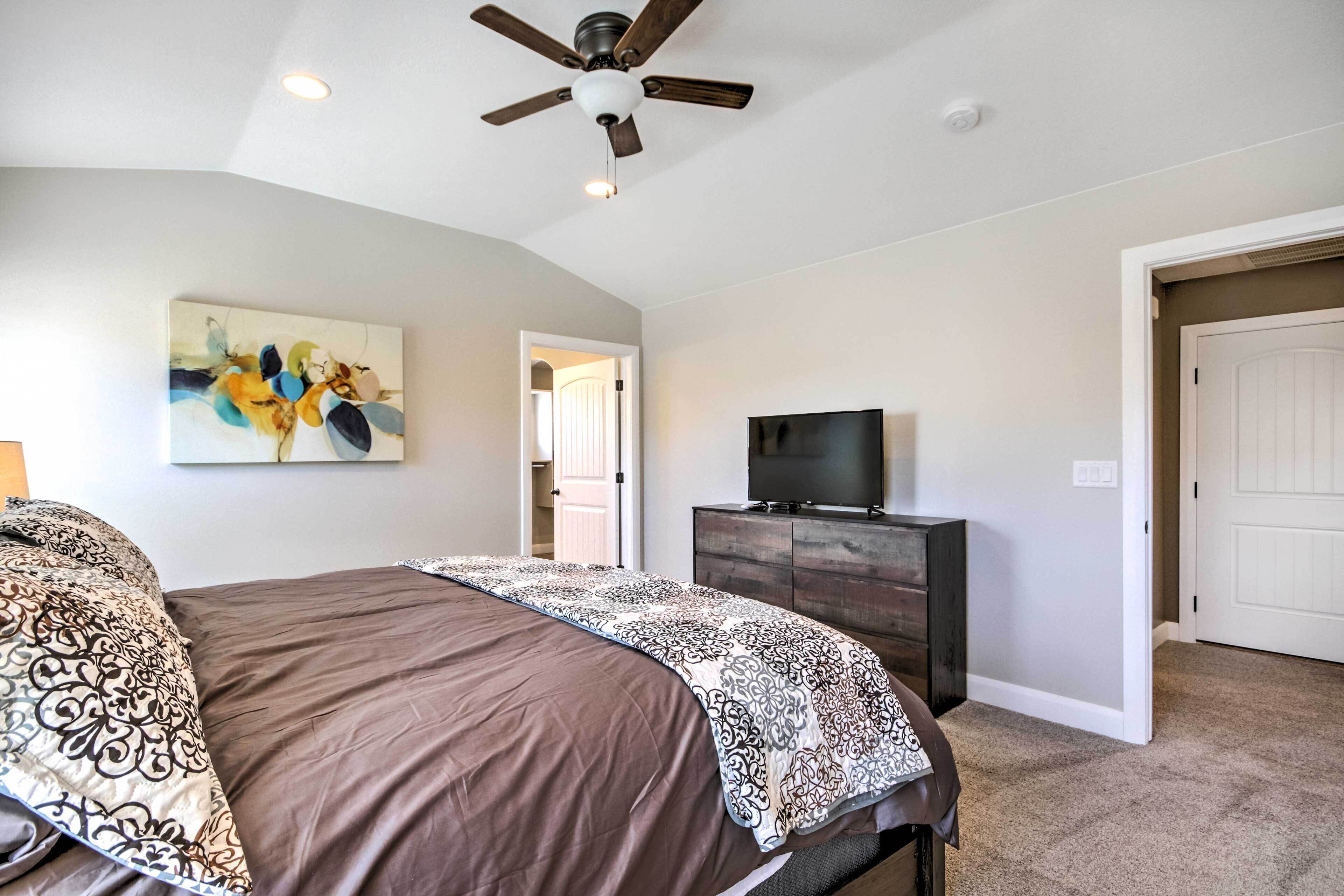 A bedroom with a bed, a ceiling fan, a TV on a wooden dresser, and a painting on the wall.