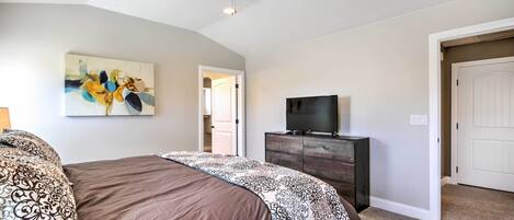 A bedroom with a bed, a ceiling fan, a TV on a wooden dresser, and a painting on the wall.