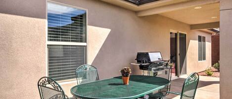 Un patio con una mesa y sillas de metal verde, una planta en maceta y una parrilla.
