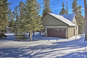A single-story house with a garage, surrounded by snow-covered ground and tall evergreen trees.