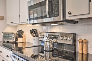 A kitchen with stainless steel appliances, including a microwave, toaster, and stove. There are wooden utensils in a holder and two wooden salt and pepper shakers on the counter. - Stylish Vilas Hideaway: Hike, Ski & Explore! (Vilas)