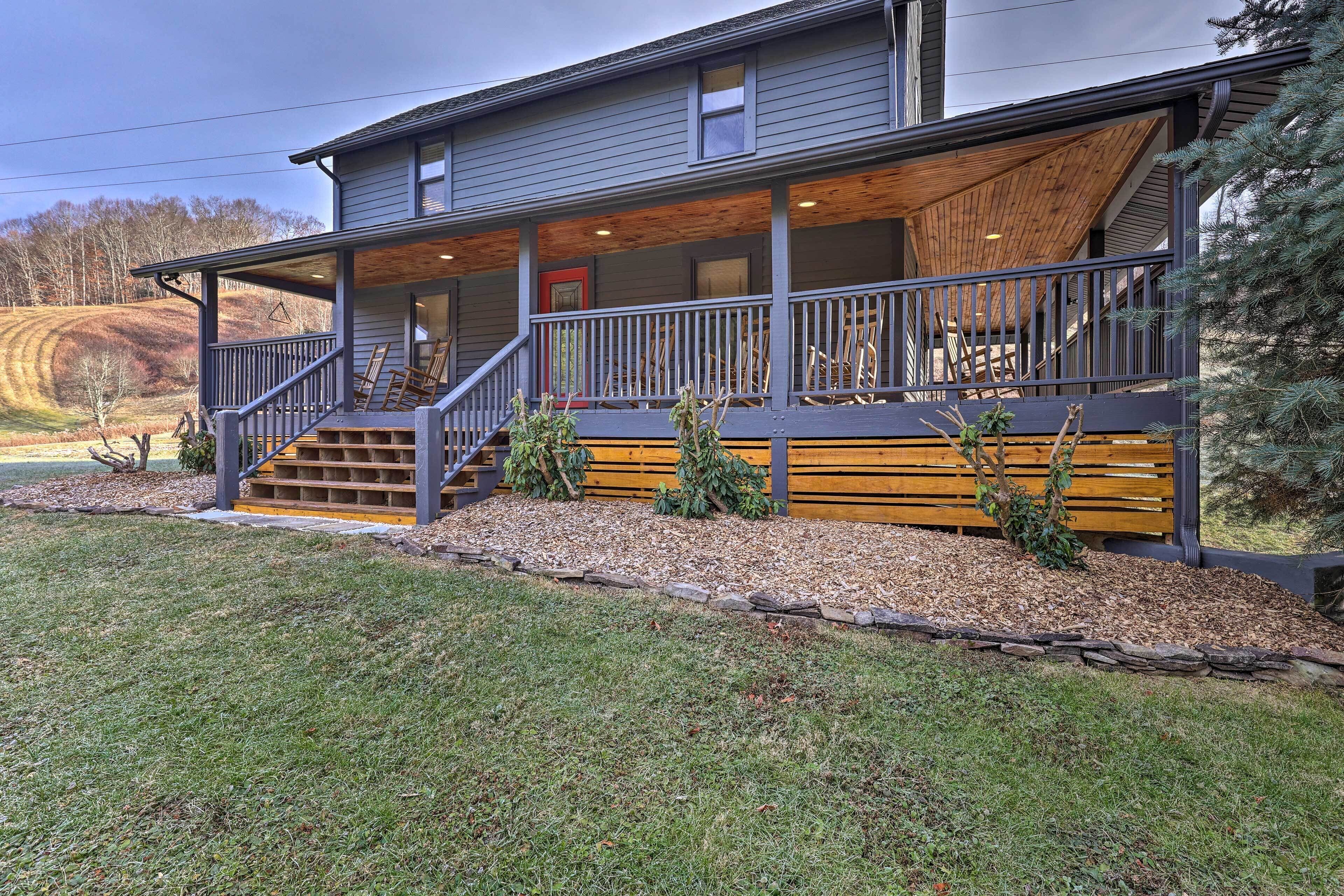 A two-story house with a covered porch, wooden steps, and a stone border.