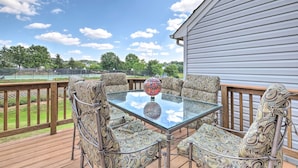 A deck with a glass table and patterned chairs, overlooking a tennis court and greenery. - Pond-view Deck + Pool Table: Woodbridge Haven! (Woodbridge)