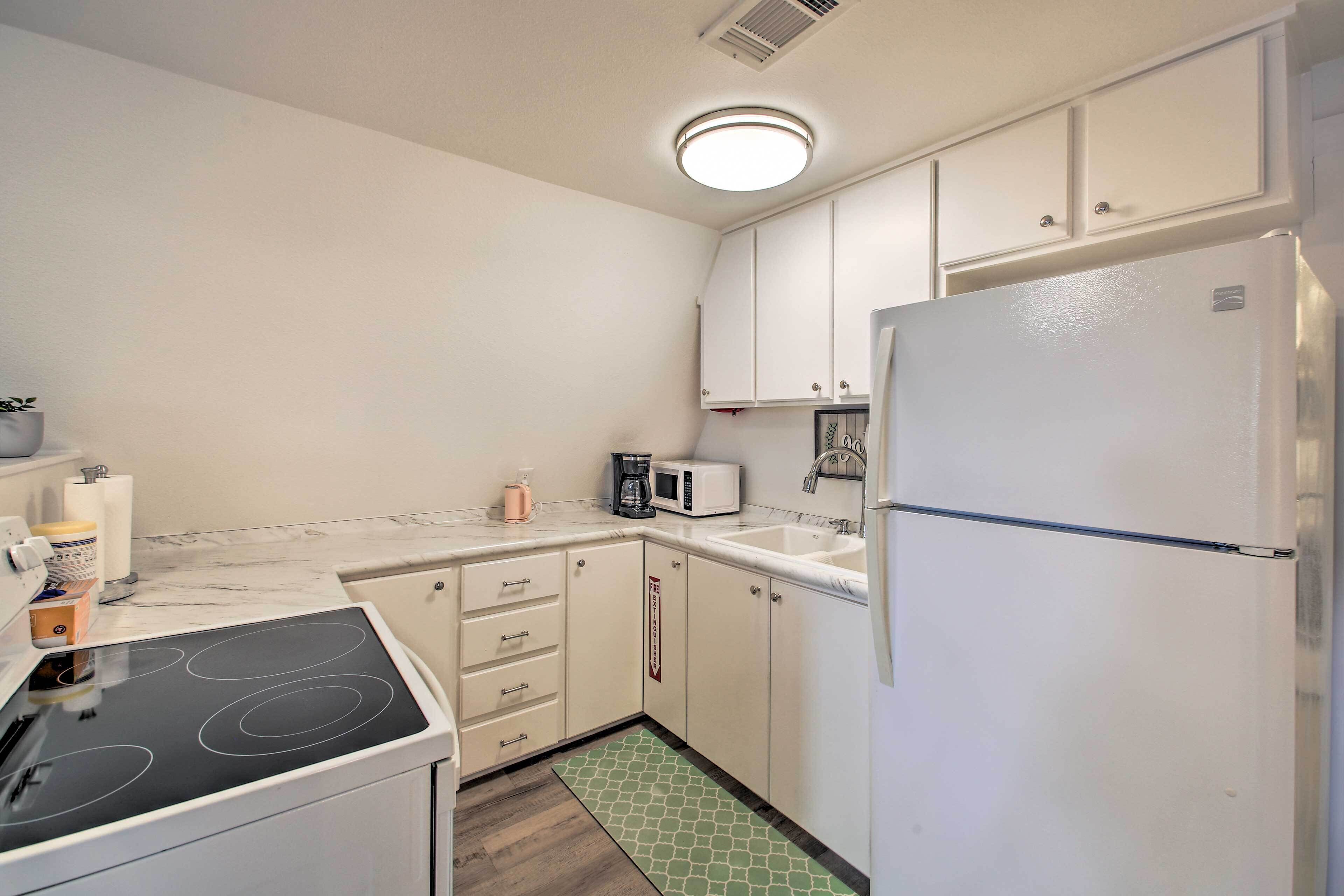 A compact kitchen with white cabinets, a white refrigerator, a microwave, a coffee maker, and a stove.