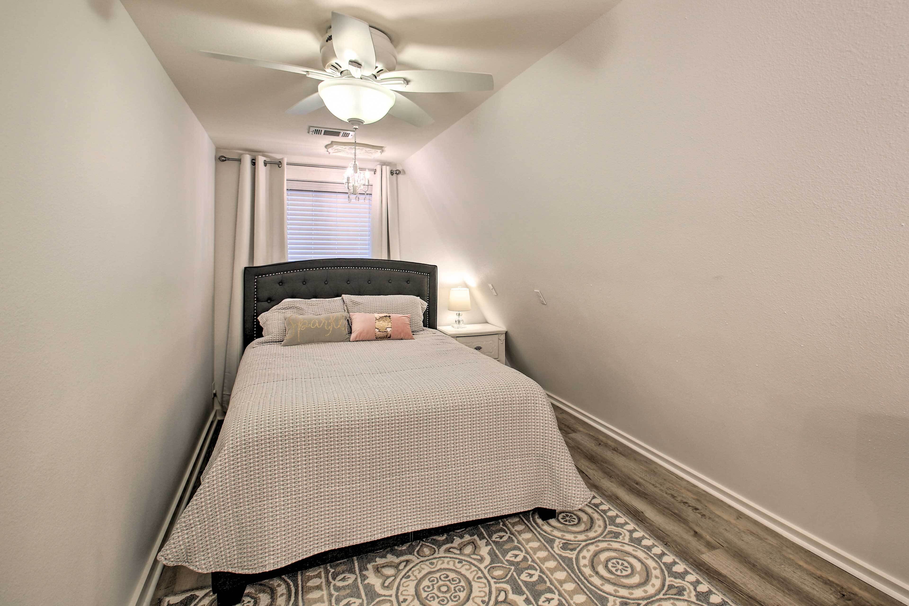 A narrow bedroom with a bed, a nightstand, a ceiling fan, and a patterned rug.