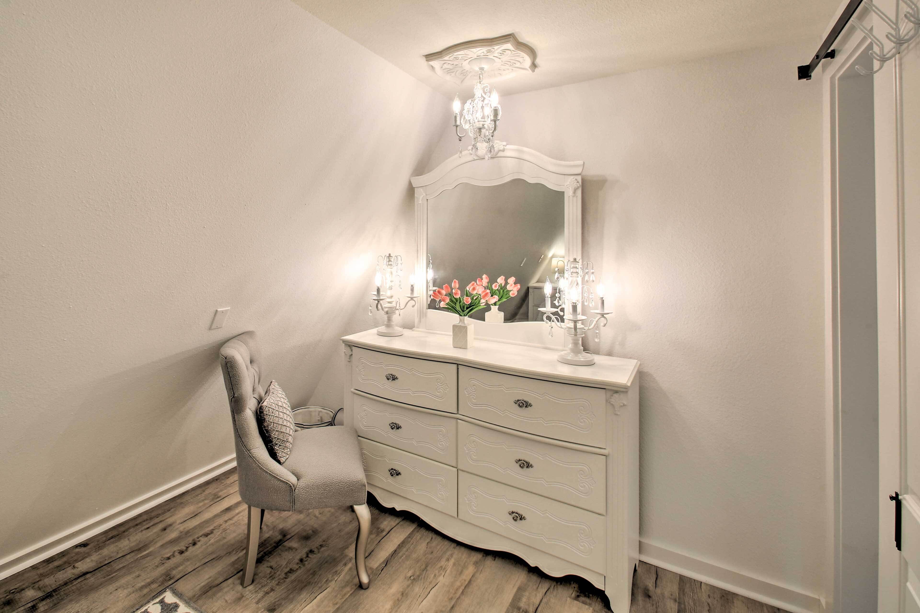 A white vanity with a mirror, two lit candles, and a vase of flowers.
