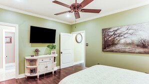 Una camera da letto con un letto, una ventola a soffitto, una TV a muro, una porta e un quadro.