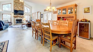 Een ruime woonkamer met een open haard, een eethoek met houten stoelen en een tafel, en een keuken met houten kastjes en een koelkast.