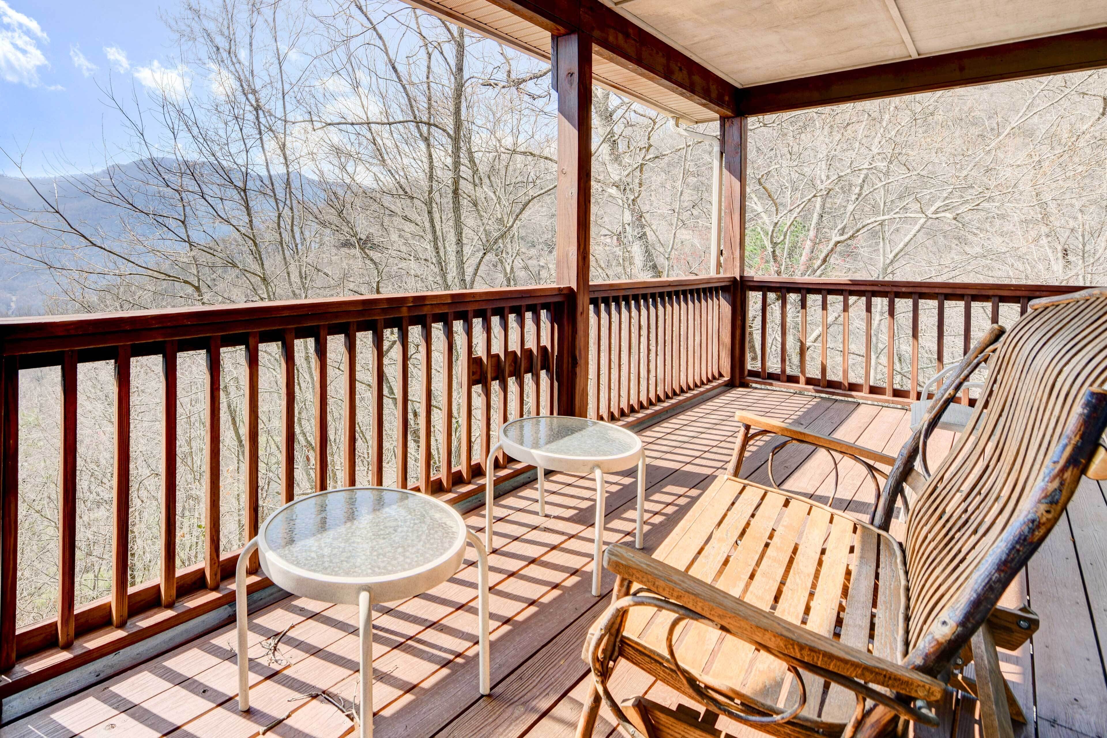 Une terrasse en bois avec une table et des chaises en verre, offrant une vue sur un paysage montagneux.