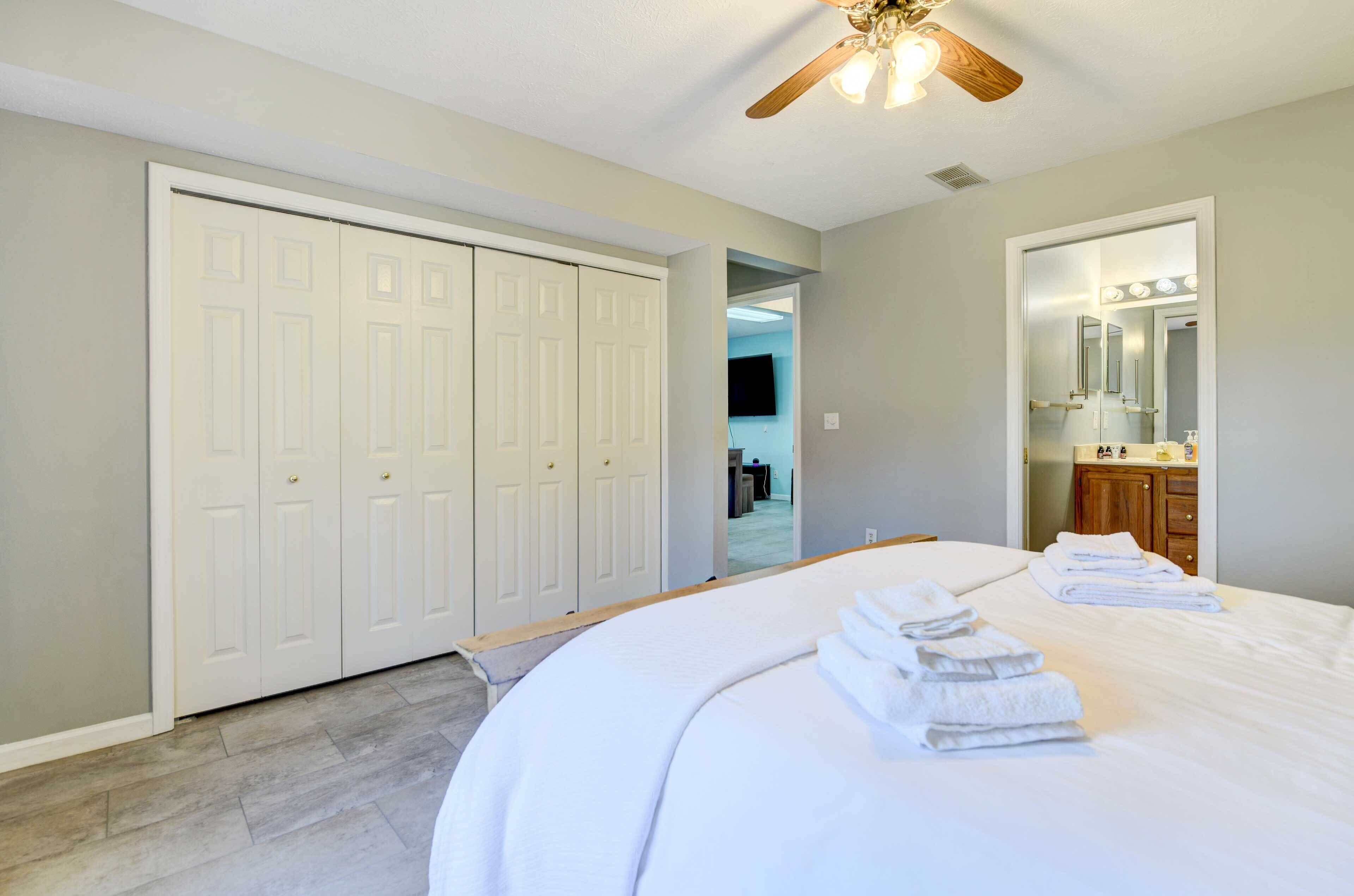 A bedroom with a large bed, a ceiling fan, a walk-in closet, and a bathroom with a vanity and mirror.