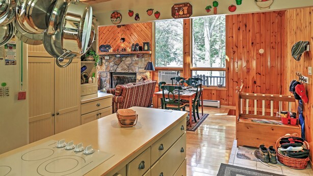 A kitchen with wooden cabinets, a stove, and hanging pots. There is a dining area with a table and chairs, and a wooden bench with boots and bags. - Stamford Lakefront Home w/ Dock & Wraparound Deck! (Stamford)