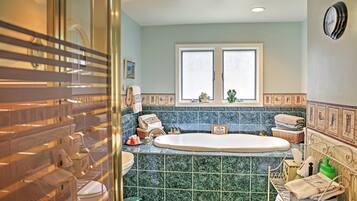 A bathroom with a large bathtub, a window, and a tiled backsplash.