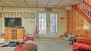 A living room with a television, wooden cabinets, a staircase, and a door with windows. - Stamford Lakefront Home w/ Dock & Wraparound Deck! (Stamford)