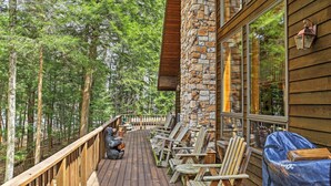 A wooden deck with chairs and a covered grill area, surrounded by a forested landscape. - Stamford Lakefront Home w/ Dock & Wraparound Deck! (Stamford)