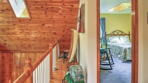 A wooden staircase leading to a bedroom with a bed, a rocking chair, and a suitcase. - Stamford Lakefront Home w/ Dock & Wraparound Deck! (Stamford)